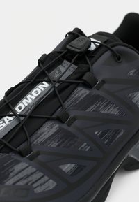 Close-up of black and gray Salomon athletic shoe with quick-pull lacing system and textured fabric upper.