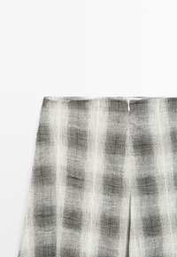 Proužkovaná černobílá látka s texturovaným vzorem; má rovný pás a skrytý zip na zadní straně.