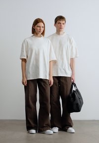 Λευκά κοντομάνικα πουκάμισα με καφέ παντελόνια σε άνετη γραμμή. Τα παπούτσια είναι λευκά αθλητικά, και ένα άτομο κρατά μια μαύρη τσάντα.