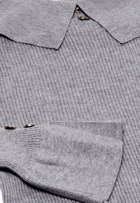 Pull en tricot côtelé gris avec un col, des accents de boutons et des manches larges avec une finition texturée.