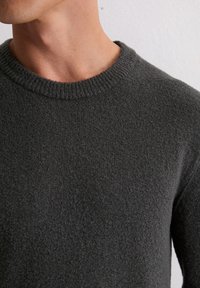 Ciemnoszara sweter z okrągłym żebrowanym dekoltem, teksturowanym materiałem i dopasowanym fasonem, prezentowany od strony ramienia.