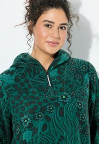 Zielony polarowy pulower z półzamkiem, zdobiony kwiatowym i lampartim wzorem. Tkanina o fakturze z miękkim wykończeniem i kapturem.