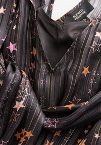Schwarzer Stoff mit vertikalen goldenen Streifen und pinken sowie orangen Sternmustern, mit einem Rockett St George Etikett innen am Halsausschnitt.