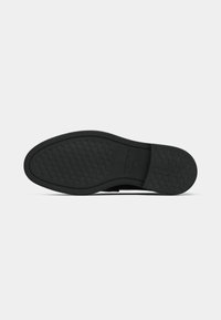 Semelle de chaussure noire avec un motif de bande de roulement texturé, des bords lisses et un logo embossé sur le côté. Design plat et flexible.