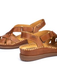 Sandalias de cuero marrón con un diseño de tiras, que presentan una textura trenzada, plantilla acolchada y una suela de plataforma elevada. Correas ajustables en el tobillo.