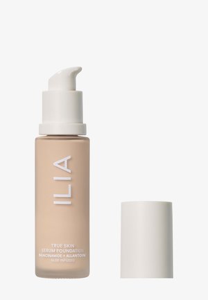 ILIA True Skin Serum Foundation i en frostad glasflaska, beige färg, med en vit pump och lock. Texten på flaskan inkluderar produktinformation.