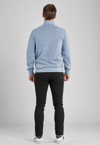 Ljusblå tröja med krage, kombinerad med svarta slim-fit jeans. Vita sneakers fulländar outfiten, sedd bakifrån.