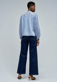 Helltürkises gestreiftes Oberteil mit einem durchsichtigen weißen Spitzenrücken, kombiniert mit dunkelblauen weiten Jeans und braunen Absatzsandalen.