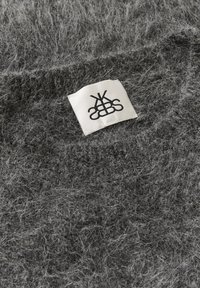 Tissu texturé gris avec une apparence floue, présentant une étiquette en tissu blanc avec un logo noir brodé dans le matériau.