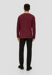 Bordowa bluzka z długim rękawem i okrągłym dekoltem, zestawiona z czarnymi spodniami. Prosty design, miękka tekstura, dopasowany krój, codzienny styl.