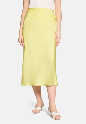 Femme portant une jupe midi en satin jaune taille haute, des sandales blanches à talons et un top blanc sans manches.