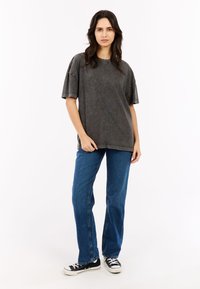 Grijze oversized t-shirt met korte mouwen, met een licht vervaagde uitstraling. Gecombineerd met blauwe rechte jeans en zwarte sneakers.