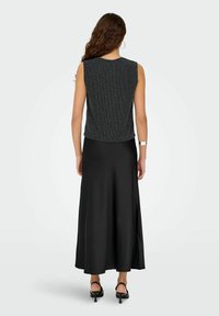 Czarny top bez rękawów z teksturowanym wzorem, zestawiony z długą, lejącą się czarną satynową spódnicą o gładkim wykończeniu i rozszerzanym dole.