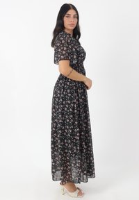 Maxi-jurk van lichtgewicht, vloeiende zwarte stof met roze bloemenpatronen. Heeft korte mouwen en een smocked taille voor een figuurlijke pasvorm.