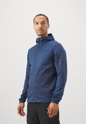 Marineblå zip-up jakke lavet af letvægtsmateriale, med hætte, to frontlynlåslommer og et logo på brystet.
