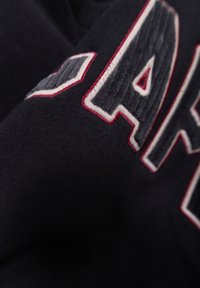 Tessuto di cotone nero con lettere ricamate in rilievo di colore grigio e bianco, con accenti rossi. La texture appare morbida e leggermente pelosa.