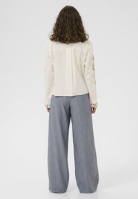 Weißes Langarmhemd mit floralem Stickereimuster an den Ärmeln, kombiniert mit blauen gestreiften weit geschnittenen Hosen. Glattes Material, taillierte Passform.