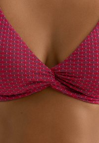 Różowy top bikini w wzory, w kształcie trójkąta z zakręconym designem z przodu. Teksturowana tkanina z małymi, kontrastującymi geometrycznymi kształtami.