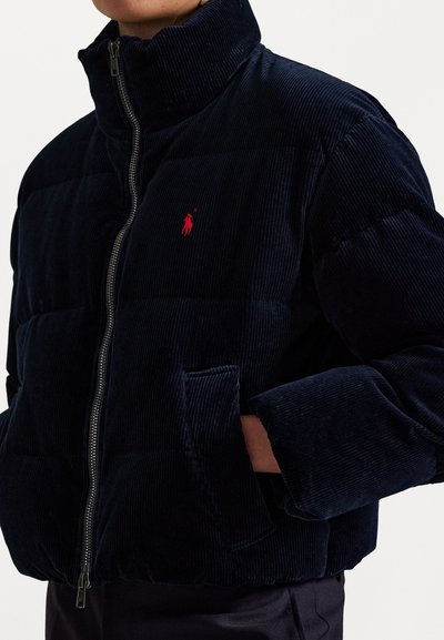 Marineblauw corduroy pufferjas met een hoge kraag, ritsafsluiting en een klein rood logo op de borst, voorzien van voorzakken.