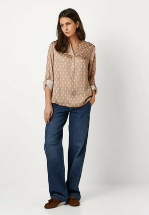 Light brown blouse with white vertical stripes, buttoned neckline, and rolled sleeves, paired with wide-leg blue denim jeans and brown shoes.