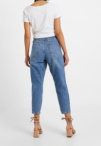 Jeans de mezclilla de cintura alta, azul claro, con pierna ajustada, que presentan bolsillos traseros y dobladillos deshilachados, combinados con una blusa blanca de manga corta.