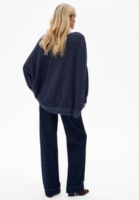 Granatowy, oversize sweter z rękawami w stylu nietoperza, wykonany z teksturowanej dzianiny, z prążkowanym dołem, w połączeniu z ciemnymi spodniami o szerokich nogawkach i brązowymi botkami za kostkę.