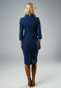 Granatowa sukienka o dopasowanym kroju z rękawami o długości 3/4, z teksturowanej tkaniny, z dopasowanym wcięciem w talii i spódnicą do kolan, w połączeniu z wysokimi brązowymi skórzanymi botkami.