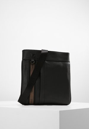 Sac bandoulière noir avec sangle réglable, bande verticale marron avec texte de la marque, et logo embossé "VJ" en haut à gauche.