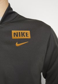 Nike svart träningströja med en ribbad krage, en djärv orange "NIKE" logotyp och en mindre orange swoosh-symbol på bröstet.