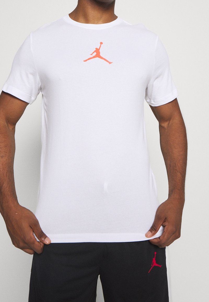 Man med vit t-shirt med korta ärmar och orange Jumpman-logotyp samt svarta shorts med matchande röd Jumpman-logotyp.