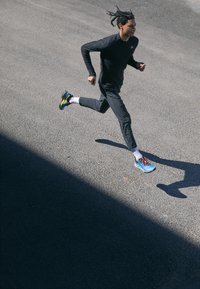Scarpe da corsa blu con accenti gialli, maniche lunghe nere e pantaloni grigi. Tessuti leggeri; posa dinamica su una superficie testurizzata.