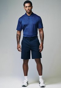 Námorně modré polo tričko s krátkým rukávem s jemnými pruhy, kombinované s námořnickými šortkami. Sportovní střih, texturovaná látka a bílé tenisky s černými akcenty.