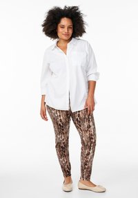Witte overhemden met knopen en een borstzak, gecombineerd met bruin slangenprint leggings. De outfit wordt aangevuld met beige flats.