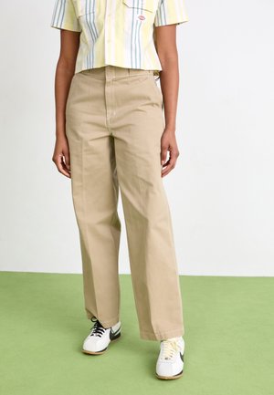 Beige wide-leg trousers in durable fabric, featuring a mid-rise waist and contrasting seams, paired with white sneakers and a striped crop top.