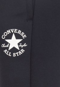 Donker marineblauwe stof met een witte cirkelvormige logo met een ster en de tekst "Converse Chuck Taylor All Star" in het midden. Zachte textuur.