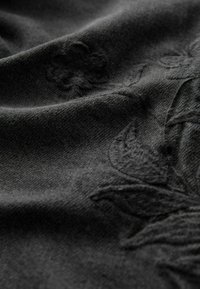 Černá tkanina s texturovaným povrchem, zdobená jemnou květinovou výšivkou. Materiál vypadá měkce a mírně heathered.