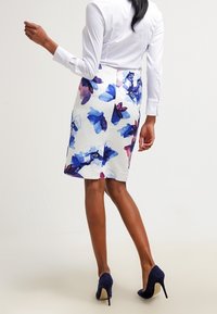 Weißer Bleistiftrock mit Blumenmuster in Blau und Lila, strukturiertem Stoff und figurbetontem Design, kombiniert mit marineblauen High Heels.