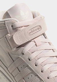 Light pink suede sneaker with round laces, velcro strap, embossed logo, and textured side detailing. Padded collar and tongue design.