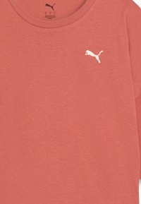 Koralfarvet bomulds T-shirt med rund hals og korte ærmer, med et hvidt Puma-logo på venstre bryst. Ensfarvet tekstur.