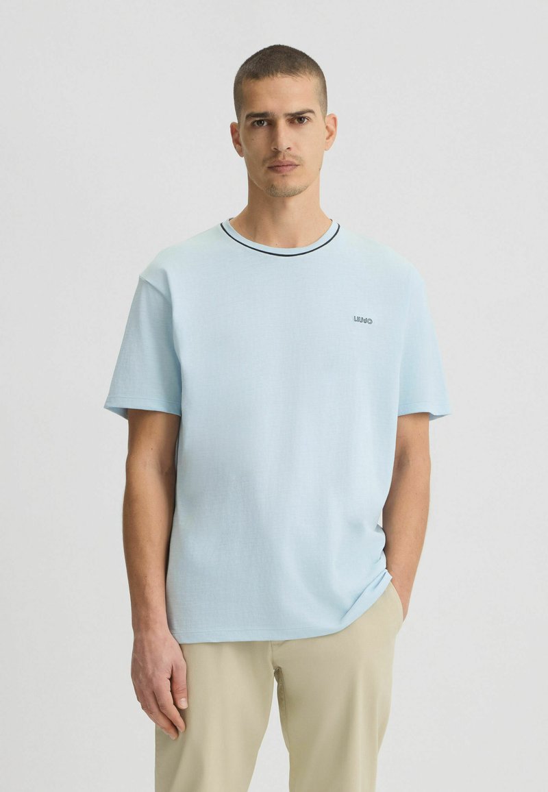 T-shirt azzurro chiaro a maniche corte con collo rotondo, bordature nere e un piccolo logo sul petto. Realizzato in tessuto morbido con una texture liscia.