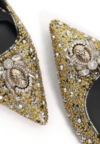 Decorative pointed-toe flats featuring a gold and silver rhinestone embellishment, intricate metallic accents, and a smooth black interior.