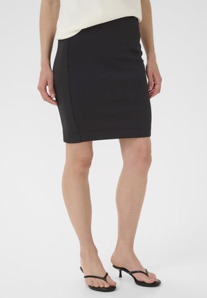 Jupe crayon noire en matière extensible, avec une coupe slim et une longueur mi-genoux. Portée avec des sandales à talons en noir.