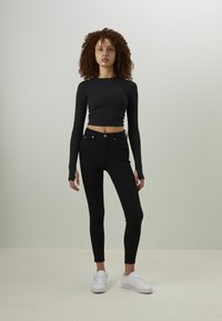Svart långärmad crop top med figurnära design, kombinerad med högmidjade svarta jeans. Vita sneakers kompletterar outfiten. Slät textur, minimalistisk stil.