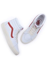 Vita hög-top sneakers i läder med ett rött sidostråk. Funktioner inkluderar vita skosnören, perforerad tå och krämfärgad gummisula.