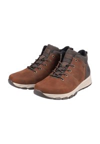 Bottines en cuir marron avec des cols rembourrés marron foncé, des lacets à l'avant et des semelles blanches texturées, inclinées à droite sur un fond blanc.