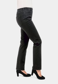 Jean noir avec une taille élastique, coupe slim et poches arrière. Associé à des chaussures à talons hauts noires, présenté sur un fond gris.