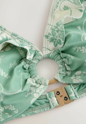 Zielony biustonosz bikini w kwiecisty wzór, z falbaniastym materiałem, złotym zapięciem i okrągłym otworem na środku. Miękki, elastyczny materiał.