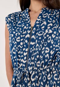Abito blu con stampa leopardata, con zip frontale, maniche corte e vita elastica. Presenta tasche sul petto e un tessuto morbido e leggero.