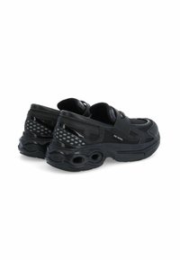 Baskets de sport noires avec une tige en maille, semelle en caoutchouc et découpes circulaires. Fermeture Velcro et accents texturés sur les côtés.
