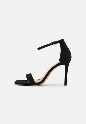 Black suede high heel sandal with a thin ankle strap, square toe, and a sleek stiletto heel, featuring a gold buckle accent.